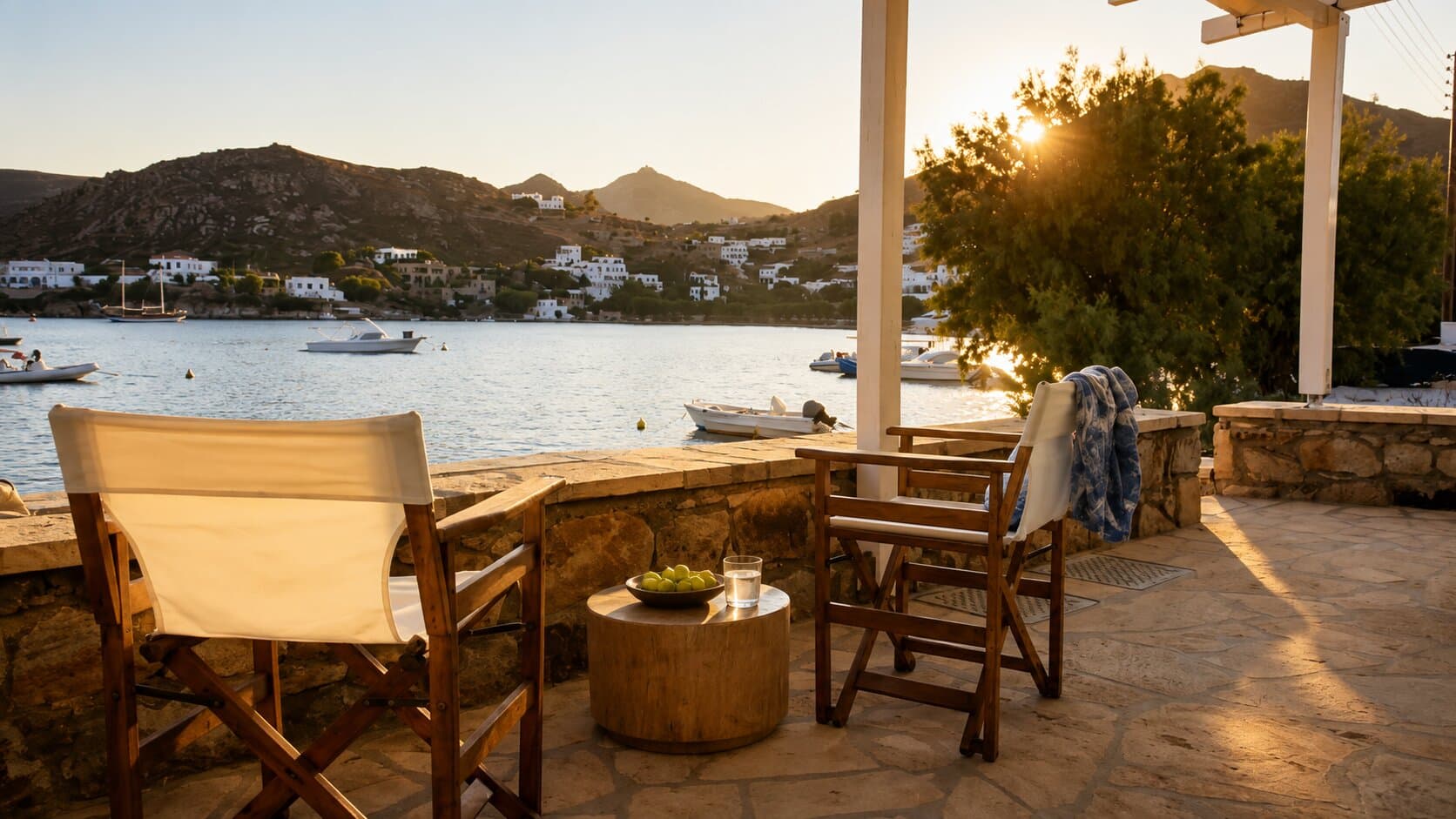 Grikos Bay at golden hour, seen from the En Plo terrace — moored boats, the far hillside and Patmos houses across the water
